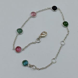 Puede incluir: Una delicada pulsera de plata con una serie de piedras preciosas de colores. La pulsera tiene un diseño de cadena con piedras redondas y pulidas en tonos rosa, verde, azul y negro. La pulsera se asegura con un cierre.