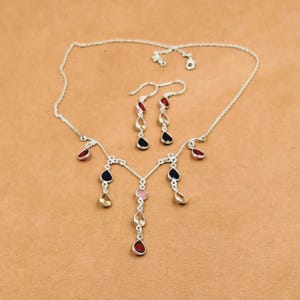 Può includere: Una collana in argento e un paio di orecchini pendenti abbinati con pietre preziose a forma di goccia nei toni del rosso, nero e giallo. La collana presenta una catena sottile con diversi accenti di pietre pendenti, ripresi dagli orecchini.
