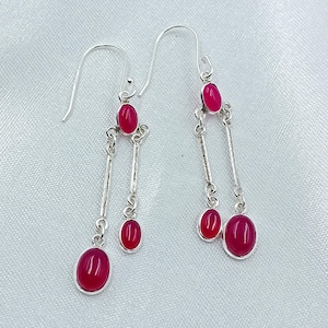 Peut inclure: Paire de boucles d'oreilles pendantes en argent avec des pierres précieuses ovales rouge rubis. Les boucles d'oreilles ont une fermeture à crochet et un design linéaire.