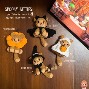 Könnte beinhalten: Vier gehäkelte Plüschkätzchen mit Halloween-Motiven. Eines trägt ein Kürbiskostüm, eines hat schwarze Fledermausflügel, eines trägt ein weißes Geisterlaken und eines trägt einen schwarzen Hexenhut mit einem Besen. Text: SPOOKY KITTIES pattern release + tester appreciation!
