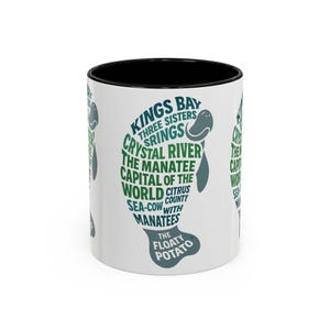 May include: White ceramic coffee mug with a black interior. The mug features a green and white design of a manatee with text that reads "Kings Bay, Crystal River, The Manatee Capital of the World, Sea-Cow with Manatees, The Floaty Potato."