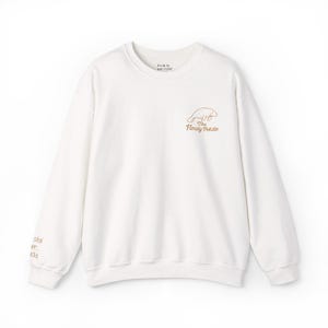 May include: Cream-coloured sweatshirt with a crew neck. The front features a small graphic of a beaver and the text "The Floofy Potato" in brown. The upper back has the text "It's ok to just FLOAT". The left sleeve has the text "stal er, ida".