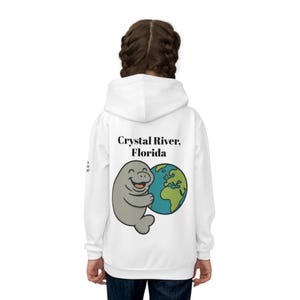 May include: White hoodie with a cartoon manatee embracing a globe. The text "Crystal River, Florida" is above the graphic. A casual, comfortable style.