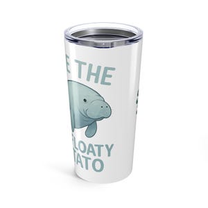 Puede incluir: Un vaso de viaje blanco con tapa plateada. El vaso presenta una ilustración de manatí de dibujos animados en tonos azules y el texto "SAVE THE FLOATY TATO" en un color azul a juego. El vaso está diseñado para mantener las bebidas calientes o frías.
