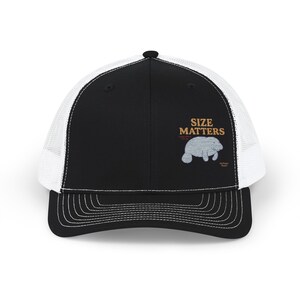 May include: Black and white trucker hat featuring the text "SIZE MATTERS" in gold. A light grey manatee is embroidered below the text. The hat has a curved peak and a white mesh back.