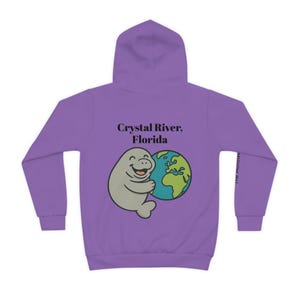 May include: A purple hoodie with a cartoon manatee hugging a globe. The text "Crystal River, Florida" is above the manatee. The Manatee logo is on the right sleeve.