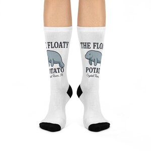 May include: White socks with black heels and toes. Each sock features a cartoon manatee illustration above the text "THE FLOATY POTATO" and the location "Crystal River, FL".