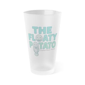 May include: A frosted glass with the words "THE FLOATY POTATO" in light blue, and a cartoon manatee illustration. The text "Crystal River, Florida" is printed below the design. The glass is empty and stands on a white surface.