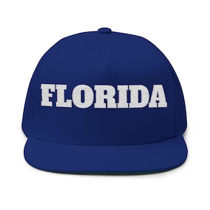 May include: A navy blue flat-peak cap featuring the white embroidered word "FLORIDA". The cap has a structured fit and a curved peak. A classic style of headwear, suitable for casual wear. The cap's brim is green.