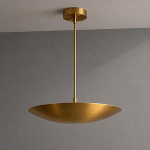 May include: A modern, gold-colored pendant light fixture. The light has a circular ceiling mount, a slender rod, and a wide, shallow bowl-shaped shade. The fixture is suspended from the ceiling, showcasing a minimalist design.