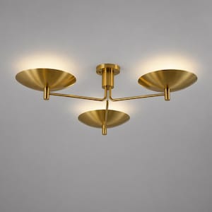 Może przedstawiać: Nowoczesna lampa sufitowa z mosiężnym wykończeniem. Lampa posiada trzy zakrzywione, tarczowate klosze, każdy z wbudowanym światłem. Oprawa jest zamontowana na centralnej łodydze.