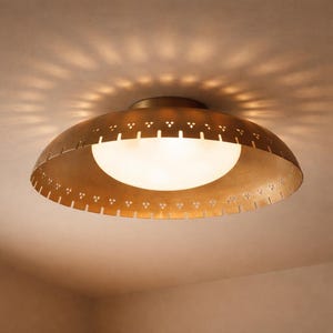 Puede incluir: Una lámpara de techo de color latón, de estilo moderno de mediados de siglo. La lámpara tiene una pantalla en forma de cúpula con patrones decorativos recortados y un globo de vidrio esmerilado. La luz proyecta un patrón en el techo.