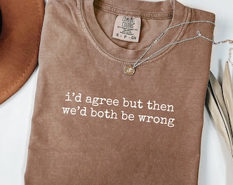 Op de afbeelding: Espresso-kleurig t-shirt met de tekst "i'd agree but then we'd both be wrong" in het wit. Een zilveren ketting met een kleine hanger is over het shirt gedrapeerd. Het shirt is van het merk Comfort Colors.