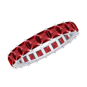 Könnte beinhalten: Ein silberner Ring mit einer durchgehenden Reihe quadratisch geschliffener, tiefroter Edelsteine. Die Edelsteine sind eng aneinander gesetzt und bilden ein Band von lebendiger Farbe. Die Metalleinfassung des Rings ist hell und poliert.