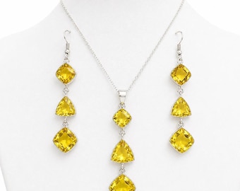 May include: A silver-toned jewelry set featuring a necklace and matching earrings. The necklace and earrings each have three yellow, faceted gemstones in a combination of square and triangular shapes. The jewelry is displayed on a white mannequin.