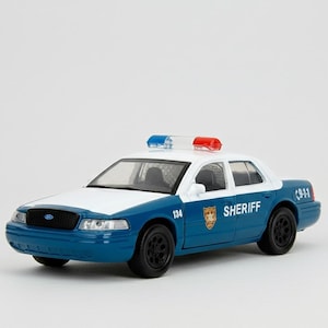 May include: A blue and white toy sheriff's car with a light bar on top. The car has the word "SHERIFF" on the side and the number "134". The car has black wheels and a black grill.
