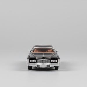 May include: A black classic car model with a tan interior. The front of the car features a chrome grill and headlights. The car is set against a plain gray background.