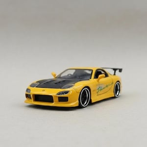 May include: A yellow model car with a black hood and spoiler. The car has black wheels with silver rims and a green and white graphic on the side. The car is a miniature replica of a sports car.