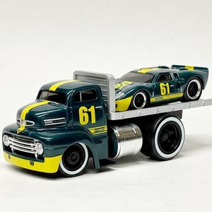 May include: A dark green Ford flatbed truck carrying a dark green and yellow Ford GT race car. Both vehicles have the number 61 and white-walled tires. The truck has a yellow stripe down the center.