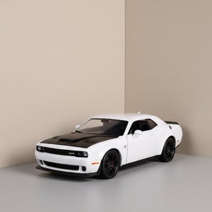 May include: A white and black model car with black wheels. The car has a black hood and a white body. The car is a Dodge Challenger.