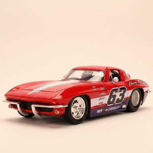 May include: A red die-cast model car with white racing stripes and the number 63 on the side. The car has chrome accents and the words "Chevy Racing" are visible. The model car is a classic sports car.