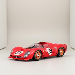 May include: A red race car model with the number 23 on the side and front. The car has gold-colored wheels and a clear windshield. The model is a replica of a classic sports car.