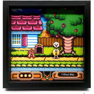 May include: A framed pixel art diorama featuring a scene from a video game. The artwork depicts a house, tree with apples, and characters on a path. The text "Village Way" is visible. The frame is black.