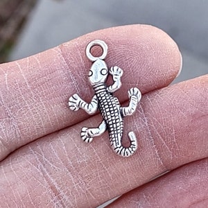 May include: Silver charm in the shape of a lizard with a loop at the top for attaching to a necklace or bracelet.