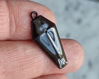 May include: A glossy black coffin-shaped pendant with a small loop at the top. The pendant has a polished surface that reflects light, and a small hole is visible near the top. The overall design is sleek and minimalist.