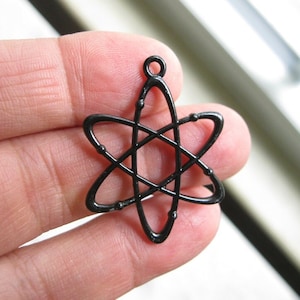 May include: Black metal atom charm pendant. The charm is shaped like an atom with a loop at the top for attaching to a necklace or bracelet.