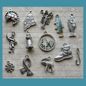 May include: A collection of silver-toned charms, including a pie, a map of Maine, a lobster, a fish, a fisherman, a lighthouse, a circular pendant with trees, a boot, a snowflake, a scarf, a moose, and a fish hook.