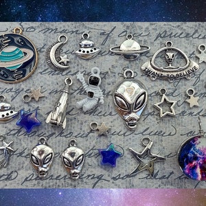 May include: A collection of silver-toned metal charms with space and alien themes. The charms include planets, stars, rockets, aliens, and a UFO with the text "I want to believe".