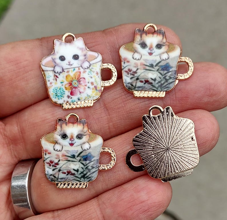 Puede incluir: Cuatro dijes con tem&aacute;tica de gatos. Cada dije presenta un gatito asom&aacute;ndose de una taza de t&eacute;. Las tazas de t&eacute; tienen dise&ntilde;os florales y bordes y asas doradas. Los dijes son de metal y son adecuados para la fabricaci&oacute;n de joyas.