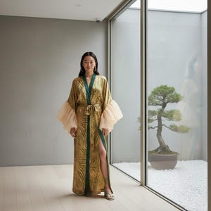 Peut inclure: Longue robe fluide avec un motif zébré doré et vert. La robe présente une bordure verte, une taille nouée et des manches roses claires et transparentes. La robe est portée avec des sandales vertes.