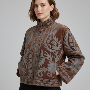 Könnte beinhalten: Eine braune Samtjacke mit Stehkragen, Reißverschluss vorne und aufwendigen grauen Blumenstickereien auf der Vorderseite und den Ärmeln. Die Jacke hat lange Ärmel und einen geraden Saum, was für eine strukturierte Passform sorgt.