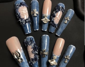 Puede incluir: Un conjunto de diez uñas artificiales largas en forma de ataúd. Las uñas presentan un diseño inspirado en el denim, con algunas uñas que muestran un efecto de denim desgastado. Otras uñas están pintadas de azul liso o color nude, y algunas tienen adornos plateados.
