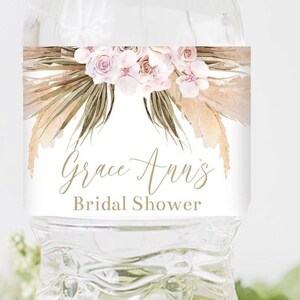 Op de afbeelding: Waterfleslabel met een bloemmotief met roze en witte bloemen, beige en groene bladeren en de tekst "Grace Ann's Bridal Shower".
