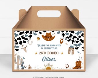 Puede incluir: Una caja de cartón marrón para recuerdos de fiesta con un tema de vaquero. La caja presenta un fondo blanco con manchas de vaca negras y azules, un sombrero de vaquero, botas y el texto "Thanks for riding over to celebrate my 2nd Rodeo Oliver."