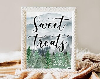 May include: A framed print with the words "Sweet Treats" in elegant script. The watercolor artwork features a forest of green trees and a mountain range in shades of gray and blue. The frame is white.