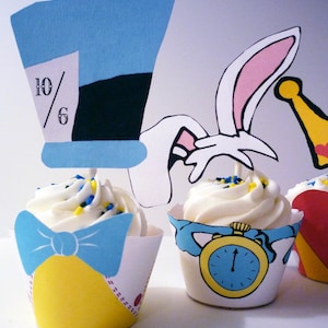May include: Three cupcakes decorated with Alice in Wonderland themed toppers. The cupcake on the left has a blue and yellow bow and a blue and white hat with the number 10/6 on it. The cupcake in the middle has a white rabbit with a pink ear and a pocket watch with blue hands. The cupcake on the right has a red heart with a gold crown.