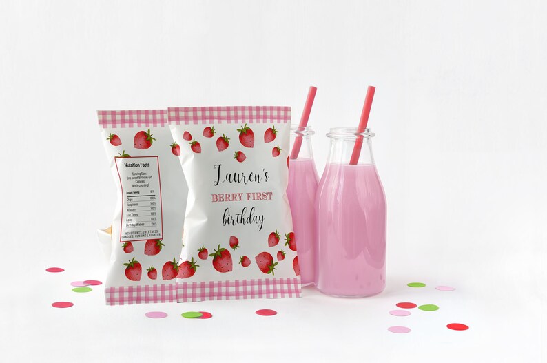 Puede incluir: Dos bolsas blancas con dise&ntilde;o de cuadros vichy rosa y blanco y fresas. Las bolsas est&aacute;n llenas de aperitivos. La bolsa de la derecha tiene el texto "Lauren's Berry First Birthday". Dos botellas de vidrio con l&iacute;quido rosa y pajitas rojas est&aacute;n delante de las bolsas. Confeti rosa, rojo y verde est&aacute; esparcido sobre la superficie blanca.