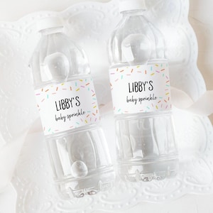 K&ouml;nnte beinhalten: Zwei durchsichtige Plastikwasserflaschen mit bunten Streusel-Etiketten, auf denen "Libby's baby sprinkle" steht.
