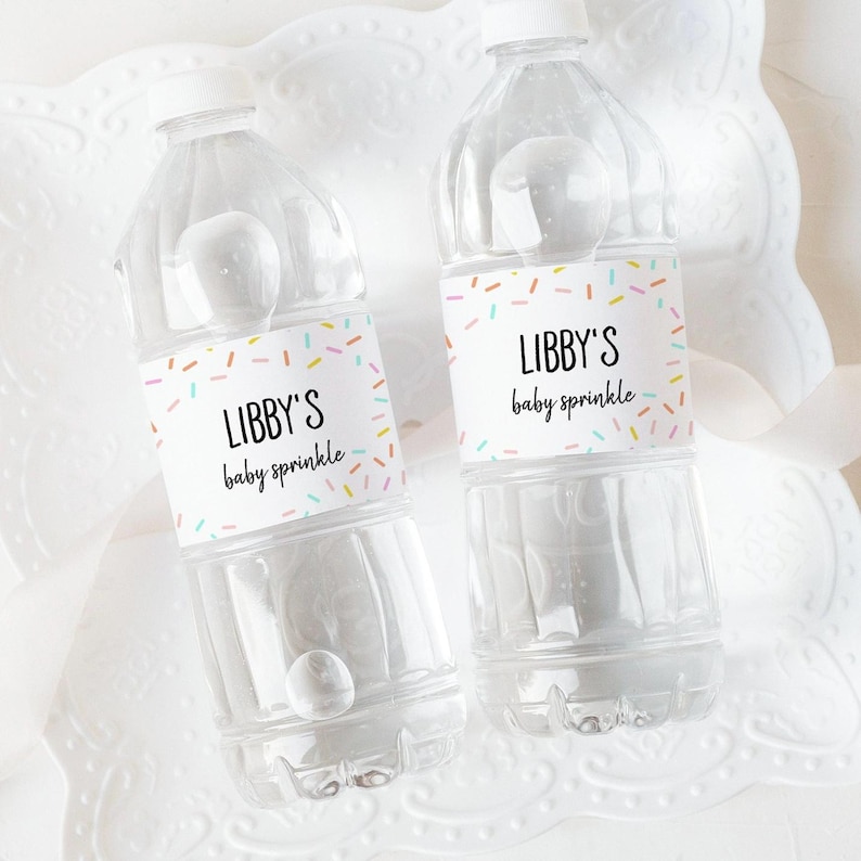 K&ouml;nnte beinhalten: Zwei durchsichtige Plastikwasserflaschen mit bunten Streusel-Etiketten, auf denen "Libby's baby sprinkle" steht.