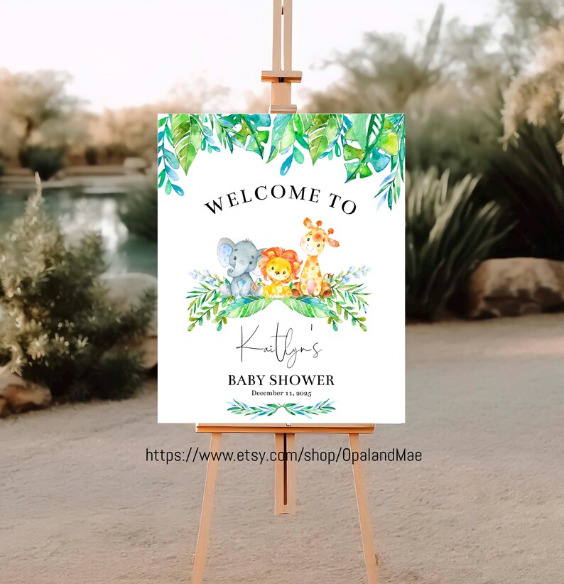 May include: Welcome to Kaitlyn's Baby Shower sign with a jungle theme. The sign features a watercolor illustration of a giraffe, lion, and elephant surrounded by green leaves. The text "Welcome to Kaitlyn's Baby Shower" is written in black with the date "December 11, 2015" below.