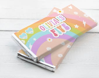 May include: Two chocolate bars wrapped in silver foil, featuring a colorful rainbow design. The wrappers have a pastel color scheme with hearts, daisies, and stars. Text on the wrapper reads "Olivia is Five."