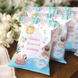 Puede incluir: Bolsas de recuerdo de fiesta blancas con temática tropical. Las bolsas presentan ilustraciones de un sol sonriente, un flotador de flamenco rosa y el texto "Olivia's Second Birthday". Otras ilustraciones incluyen una rodaja de sandía y un flotador de unicornio.
