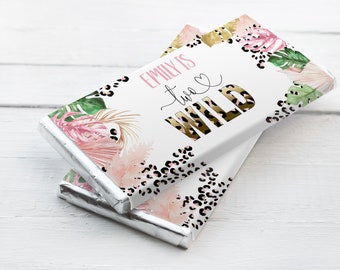 Könnte beinhalten: Zwei Schokoladenriegel-Verpackungen mit einem tropischen Design in Pink, Gold und Grün. Der Text auf der Verpackung lautet "Emily is two wild" mit einem Herzsymbol.