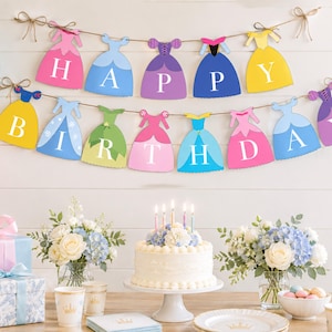 May include: A two-tiered banner featuring colorful dress-shaped cutouts, each displaying a single white letter to spell out HAPPY BIRTHDAY. The dresses are in shades of pink, blue, purple, yellow, and green, all strung together on brown twine.