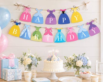 Può includere: Una ghirlanda a due livelli con sagome colorate a forma di vestito, ognuna con una lettera bianca per comporre la scritta HAPPY BIRTHDAY. Gli abiti sono nei toni del rosa, blu, viola, giallo e verde, appesi a uno spago marrone.