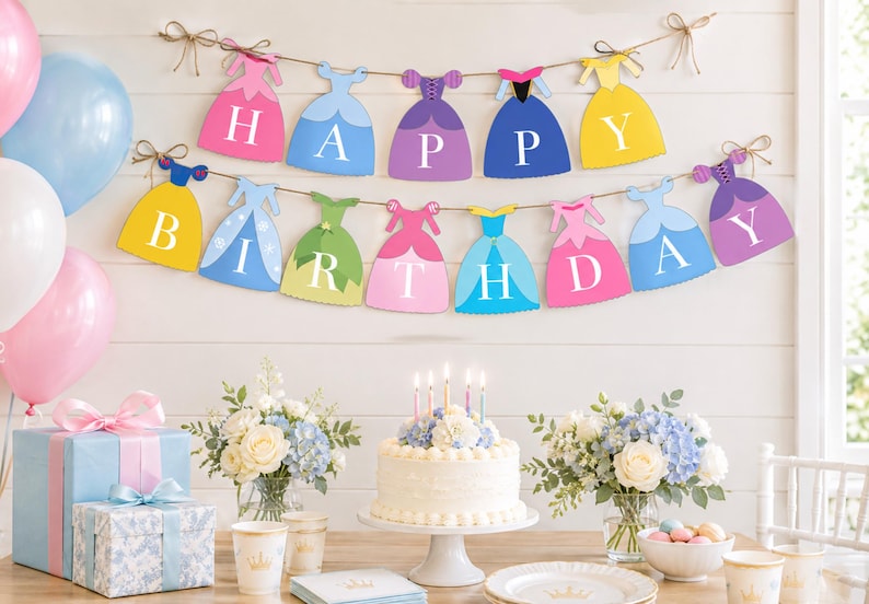 May include: A two-tiered banner featuring colorful dress-shaped cutouts, each displaying a single white letter to spell out HAPPY BIRTHDAY. The dresses are in shades of pink, blue, purple, yellow, and green, all strung together on brown twine.
